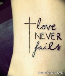 Фото тату на запястье: крест и надпись 'love NEVER fails' каллиграфическим шрифтом. Черно-белый рисунок татуировки, выполненный в минималистичном стиле.