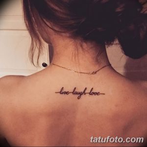 Фото тату на спине: надпись 'live laugh love' каллиграфическим шрифтом. Черно-серый рисунок татуировки, расположенный между лопатками.