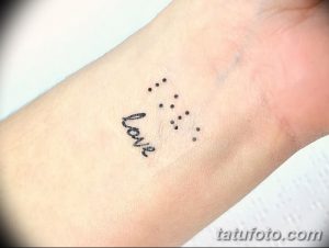 Фото тату на запястье: надпись 'love', написанная обычным шрифтом, и точки, расположенные над ней, имитирующие двоичный код. Эскиз татуировки символизирует любовь в современном мире.