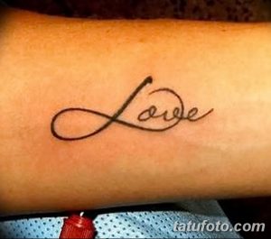 Фотография татуировки надписи 'Love' на предплечье, выполненной тонкой черной линией. Минималистичный дизайн.