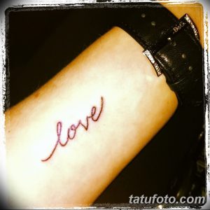 Фотография простой татуировки надписи 'love' на запястье, выполненной тонкой красной линией. Минималистичный дизайн.