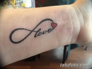 Фото тату бесконечности с маленьким сердцем и надписью 'Love' на запястье. Черно-белый рисунок татуировки.