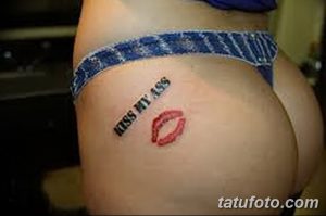 Фото небольшой татуировки с изображением красных губ и надписи 'Kiss My Ass' на женской ягодице.