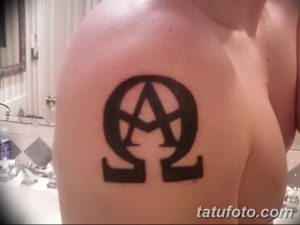 Фото минималистичной татуировки на плече с изображением символа Альфа и Омега, выполненного в черном цвете.