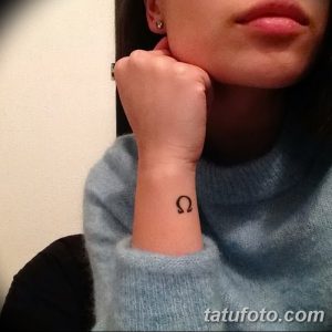Фото тату: маленькая черная татуировка греческой буквы Омега на запястье девушки. Простой и элегантный дизайн.