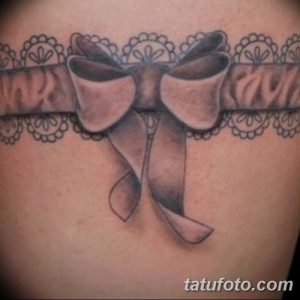 Фото тату: черная татуировка подвязки с кружевным узором, расположенная на теле женщины, выполненная в реалистичном стиле.