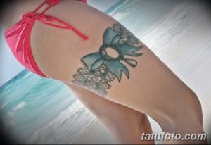 Фотография татуировки подвязки с бантом, выполненной в голубых тонах на бедрах девушки.