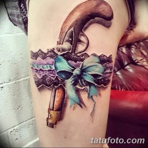 Фотография татуировки подвязки с пистолетом, выполненной в ярких цветах на руке девушки.