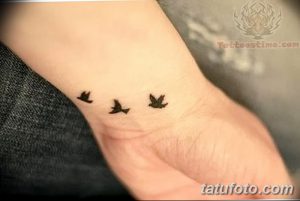 Фото тату с изображением нескольких маленьких птичек на запястье. Птицы выполнены черными чернилами, рисунок простой и лаконичный.