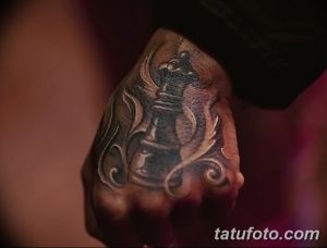 Фото татуировки на руке: шахматная королева в темных тонах с элементами пламени и завитушек. Мистический и загадочный дизайн.