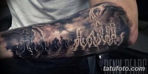 Фото тату на руке: детализированное изображение шахматной партии с фигурами и руками, играющими в шахматы, выполненное в черно-серых тонах.