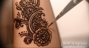 Фото тату хной: детализированный узор с цветочными и геометрическими элементами на руке, мастер наносит хну.