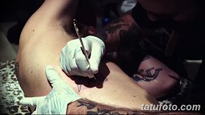 Фото тату: мастер тату в перчатках наносит рисунок на кожу клиента. Виден процесс нанесения татуировки, инструменты и детали работы.