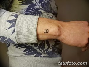 Фото минималистичной татуировки на запястье с изображением числа '10', выполненного простыми линиями.