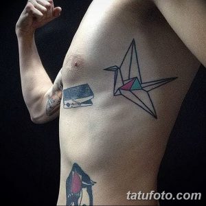 Фотография мужского торса с татуировкой в стиле оригами. Изображен бумажный журавль, выполненный в геометрическом стиле с использованием черных линий и цветных акцентов.