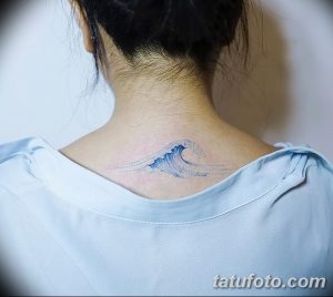 Фото минималистичной татуировки в виде волны, расположенной на затылке девушки. Использованы нежные голубые оттенки.