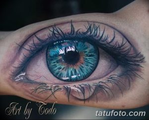 Фотография реалистичной татуировки глаза с ярким голубым радужным оттенком, выполненной на руке. Детализированный рисунок тату.