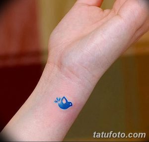 Фото минималистичной татуировки маленькой голубой птички на запястье женской руки. Простой и изящный рисунок.