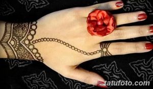 Фото тату мехенди на руке, с узором, дополненным красным цветком, имитирующим кольцо. Оригинальное и стильное решение.