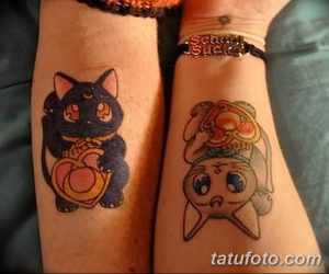 Фото тату двух милых котят на запястьях. Один кот черный с оранжевым бантиком, другой - белый с розовым. Яркие цвета и мультяшный стиль.