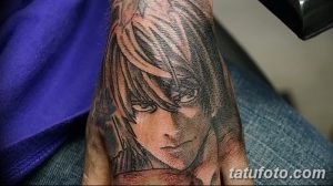 Фото тату на руке с изображением L из аниме Death Note. Рисунок татуировки выполнен в черно-серой гамме с использованием штриховки и теней для создания реалистичного эффекта.