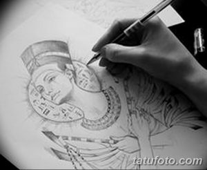 Фотография эскиза татуировки с изображением Клеопатры, выполненного карандашом. Рука мастера рисует детали лица и украшений.