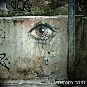 Черно-белый эскиз тату плачущего глаза, нарисованного на бетонной стене с граффити.