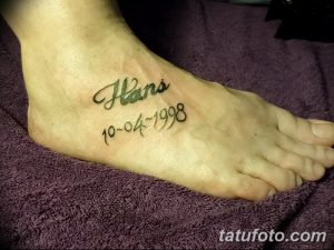 Фото тату с именем 'Hans' и датой '10-04-1998', выполненным на стопе. Нежная и личная татуировка.