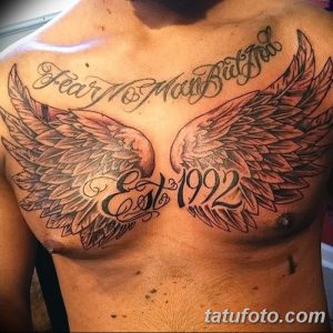 Фото большой татуировки на груди с крыльями, текстом "Fear My Mark But Feel God" и датой "Est 1922". Черно-серый рисунок, реалистичный стиль, символ веры и силы.