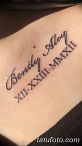 Фото тату на груди с надписью 'Bentley Alex' и датами в римских цифрах. Черно-белый рисунок татуировки, выполненный каллиграфическим шрифтом.