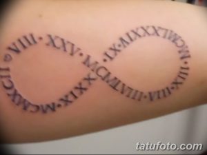 Фото тату: черная татуировка в виде символа бесконечности, внутри которого расположены римские цифры на руке. Символичное и стильное изображение.