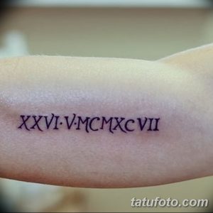 Фото тату: черные римские цифры 'XXVI.V.MCMXCVII' на запястье, выполненные тонкой линией. Минималистичный рисунок татуировки.