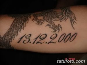 Фото тату с изображением дракона и датой '13.12.2000', выполненное в черно-серых тонах на предплечье. Детализированный рисунок татуировки с элементами восточного стиля.