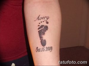 Фото тату с отпечатком детской ножки и именем 'Avery' на предплечье. Черно-серый рисунок татуировки, выполненный в минималистичном стиле.