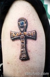 Фото тату на руке: сложная и детализированная татуировка, сочетающая Анкх и Глаз Гора, выполненная в реалистичном стиле с использованием теней и текстур.