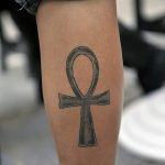 Фото минималистичной татуировки Анкха, выполненной в черно-серых тонах на ноге человека.