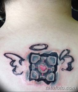 Фото тату: Татуировка на груди с изображением Companion Cube из игры Portal, с добавлением нимба и сердца. Черно-серые тона.