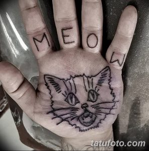 Фото татуировки кошачьей морды на ладони и надписи "MEOW" на пальцах. Рисунок выполнен в черном цвете, с использованием простых линий и забавного выражения морды кота.