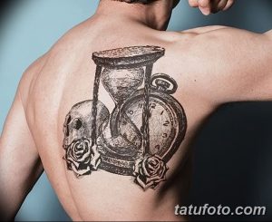 Фото тату на лопатке: старинные часы, череп и две красные розы, выполненные в реалистичном стиле черными чернилами.