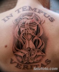 Фото тату песочные часы с костями и надписью 'In Tempus Veritas' на спине. Черно-серый рисунок, готический стиль, мрачная атмосфера.