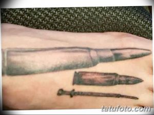 Фотография татуировки на руке: патрон и кинжал, расположенные рядом. Цветной рисунок с элементами реализма и традиционной татуировки.