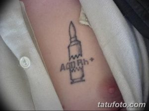 Минималистичная татуировка пули с указанием группы крови (A(II) Rh+). Черно-белый рисунок на руке, выполненный в простом стиле.