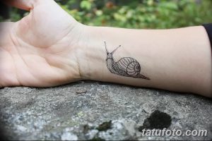 Фото тату: тонкая татуировка улитки на запястье. Минималистичный рисунок татуировки в стиле лайнарт, выполненный тонкими черными линиями.