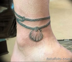 Фото тату: татуировка раковины, подвешенной на веревке, на лодыжке, выполненная в серой гамме. Идеально для любителей морской тематики и минималистичных татуировок.
