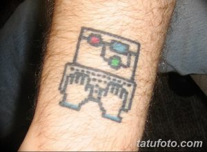 Фото тату в стиле 8-bit с изображением робота на руке. Пиксельный рисунок в сине-черных тонах, напоминающий старые видеоигры.