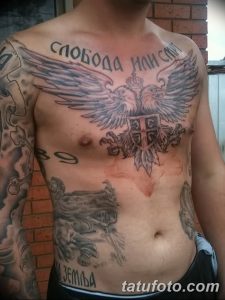 Фото масштабной татуировки на груди и плечах с изображением орла с расправленными крыльями, надписью и другими элементами, выполненное в черно-серых тонах.