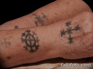 Фото тату с маленькими славянскими символами на запястье. Чёрный рисунок татуировки в виде крестов и других знаков, выполненный в минималистичном стиле.