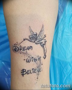 Фото тату феи Tinkerbell, держащей волшебную палочку, с надписью "Dream, Wish, Believe" на руке, выполненное в черно-белой гамме.