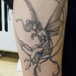 Фото тату феи, сидящей на луне, выполненное в черно-серых тонах с детальной проработкой крыльев и одежды. Изящный рисунок татуировки.