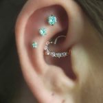 Фото уха с несколькими пирсингами, украшенными маленькими бирюзовыми камнями. Изящный и женственный дизайн.